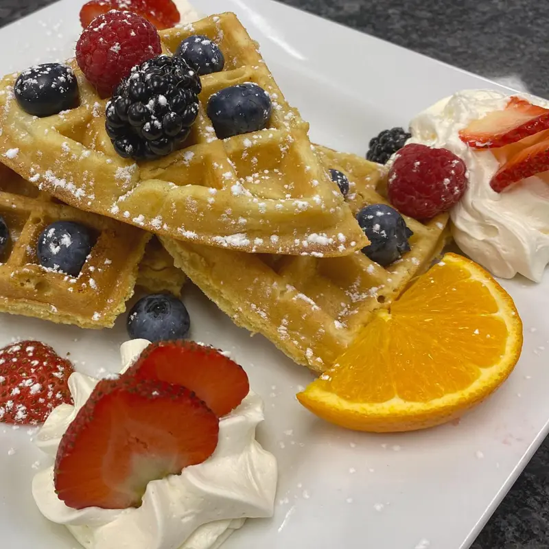 Waffles with fresh berries, whipped cream and orange slice