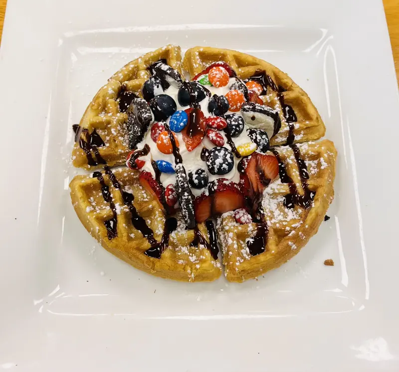 Belgian waffle topped with whipped cream, berries and chocolate drizzle