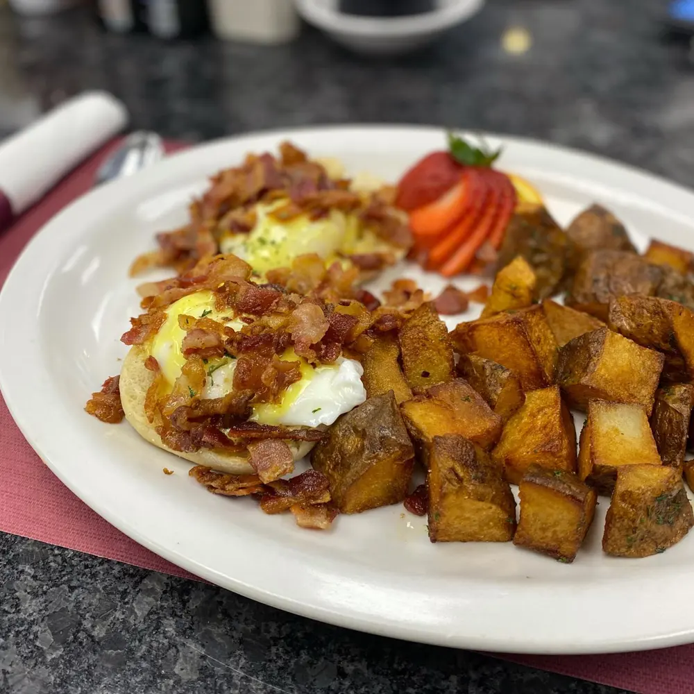 Eggs benedict with home fries and a fresh strawberry